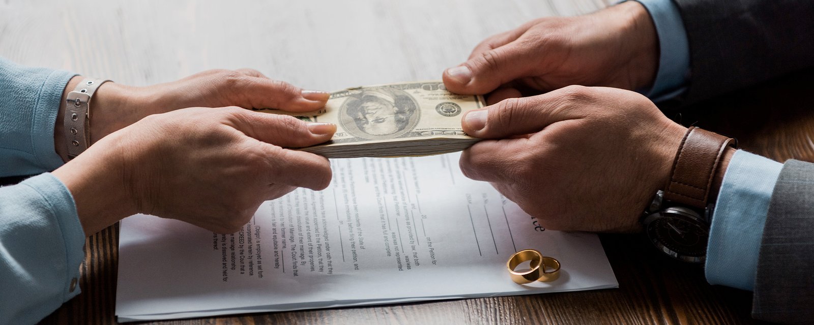 partial view of lawyer and client holding dollar banknotes above divorce decree with wedding rings 
